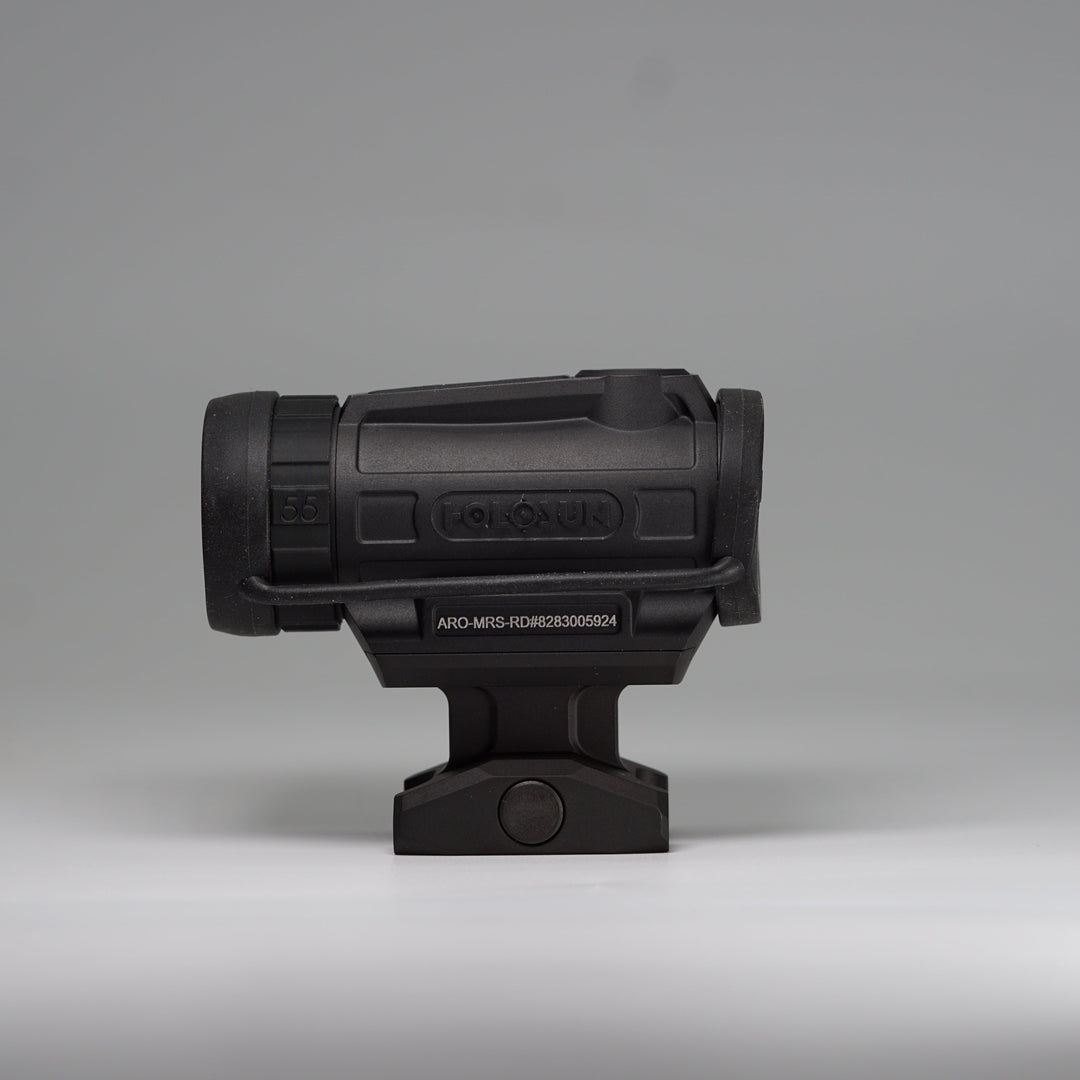 A black tactical-style ARD device on a Holosun Optic with a cylindrical body, perforated front hex pattern, and mounting base, shown using the OM dust cover. Photographed on a smooth light gray studio background. 