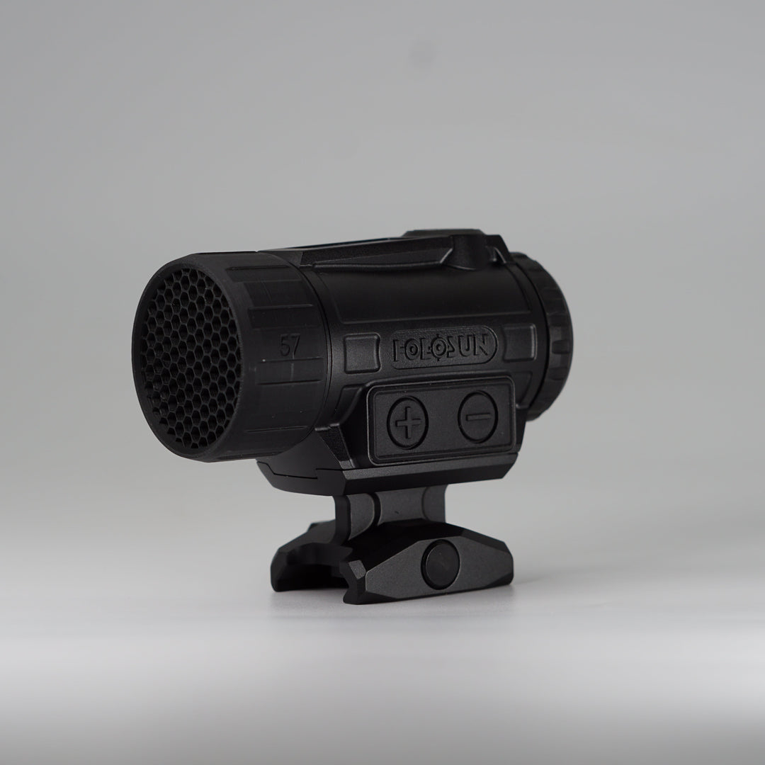 A black tactical-style ARD device with a cylindrical body, perforated front hex pattern, on a holosun red dot optic and mounting base, photographed on a smooth light gray studio background. 