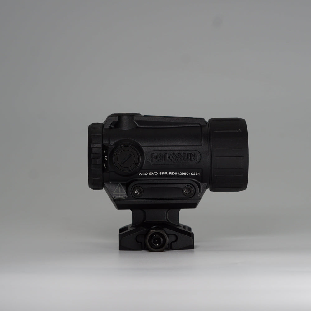 A black tactical-style ARD device with a cylindrical body, perforated front hex pattern, on a holosun ARO red dot optic and mounting base, photographed on a smooth light gray studio background. 