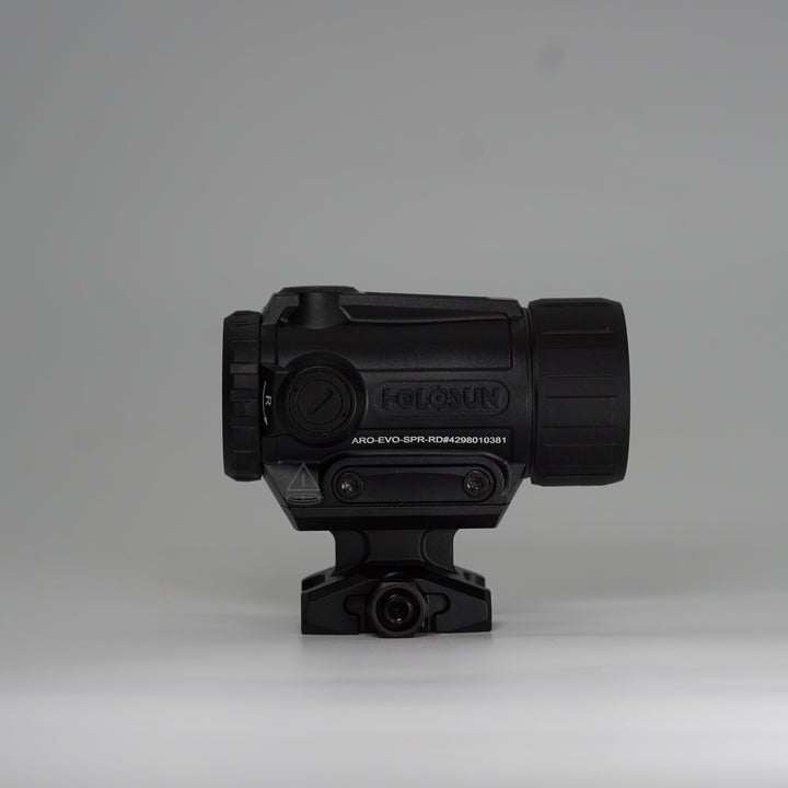 A black tactical-style ARD device with a cylindrical body, perforated front hex pattern, on a holosun ARO red dot optic and mounting base, photographed on a smooth light gray studio background. 